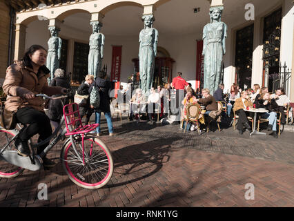 Utrecht, Niederlande, am 15. Februar 2019: Mädchen auf dem Fahrrad geht Outdoor Cafe im niederländischen Utrecht in den Niederlanden am sonnigen Wintertag Stockfoto