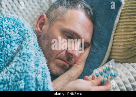 Ältere Menschen, die unter Depressionen leiden, liegt leider mit einer Decke auf sein Bett fallen und hält Antidepressiva in seiner Hand. Stockfoto