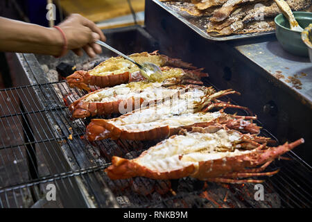 Verkäufer ist Kochen Hummer auf dem Grill auf der Street Food Market in Bangkok in Thailand. Er setzt Soße auf Sie. Closeup horizontale Foto. Stockfoto