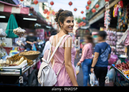 Glückliches Mädchen in einem gestreiften rosa Kleid Spaziergänge auf dem asiatischen Markt bei der Feier der Neujahrsfest in Bangkok, Thailand. Sie hat eine leichte b Stockfoto