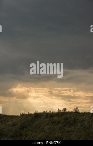 Frühling Landschaft der grasbewachsenen Hügel gegen einen dramatischen Sonnenuntergang Himmel mit Fluffy Clouds und volumetrischen Licht durch Sie Stockfoto