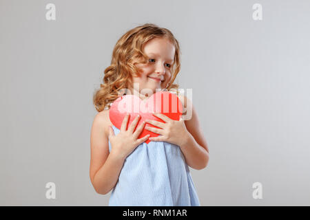 Portrait einer entzückenden kleinen Kind Mädchen Knuddel ein rotes Herz aus Papier. Grauer Hintergrund, Studio Stockfoto