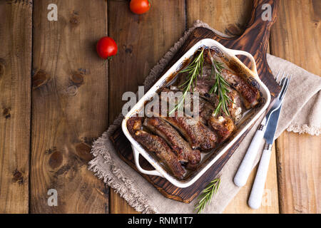 Gegrillte Schweineribs. Fleisch mit Gewürzen und Kräutern in Gerichten auf Holzgrund. Mittagessen Barbecue mit Salat und Sauce. Freier Speicherplatz für den Text Stockfoto