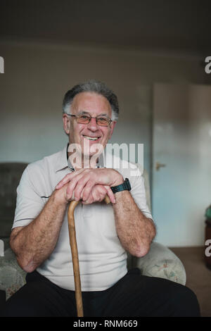 Porträt einer fröhlichen älteren Mann mit seinem Spazierstock im Wohnzimmer seines Hauses. Stockfoto