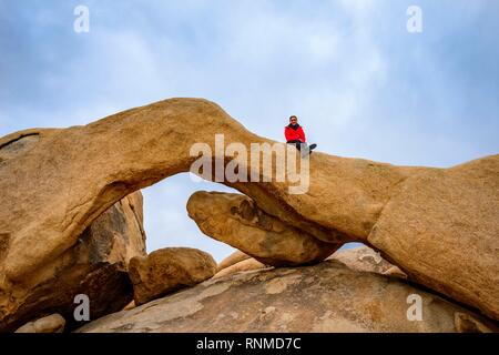 Junge Frau sitzt auf Arch Rock, Rock Arch, monzogranite Formation, Arch Rock Nature Trail, White Tank Campground Stockfoto