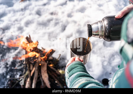 Gießen heißes Getränk aus der Thermoskanne auf einem Campingplatz. Person warm in der Nähe von einem Lagerfeuer, point-of-view Shot Stockfoto