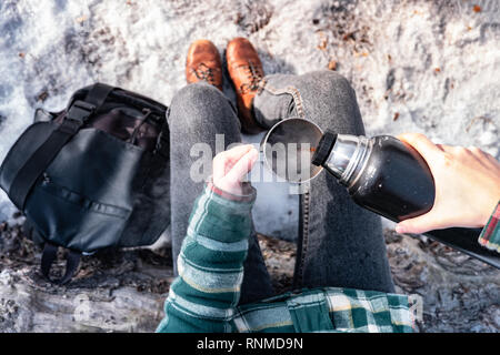 Gießen heißes Getränk aus der Thermoskanne auf einem Campingplatz. Person im Winter Forest während einer Wanderung warm, point-of-view Shot Stockfoto