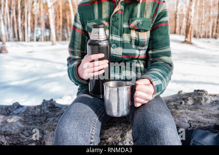 Gießen heißes Getränk aus der Thermoskanne auf einem Campingplatz. Person im Winter Forest während einer Wanderung warm Stockfoto