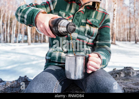 Gießen heißes Getränk aus der Thermoskanne auf einem Campingplatz. Person im Winter Forest während einer Wanderung warm Stockfoto