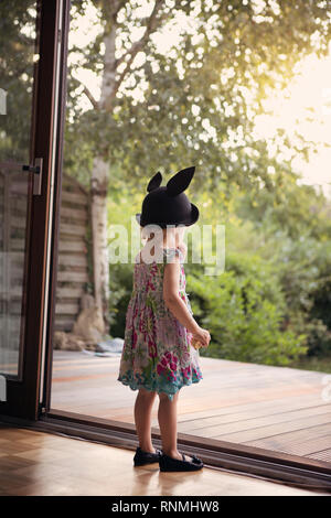 Kleines Mädchen mit Hase hat, zögernd stand neben einer offenen Terrasse Tür Stockfoto