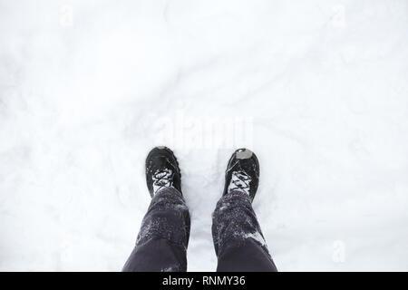 Männliche Füße in schwarze Schuhe stehen auf verschneiten Boden, erste Person anzeigen Stockfoto