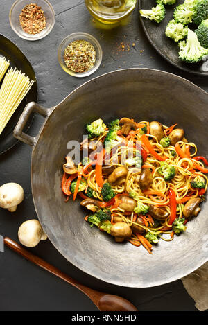 Unter Rühren braten, Nudeln mit Gemüse im Wok Pfanne auf schwarzen Stein Hintergrund. Vegan Vegetarisch Wokgemüse mit Eiernudeln. Ansicht von oben, flach Stockfoto