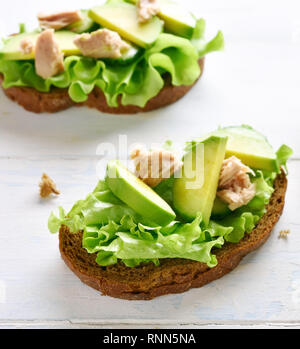 In der Nähe von Thun Sandwiches mit Avocado und Salatblätter auf hellem Holztisch. Lecker Thunfisch Brötchen zum Frühstück. Gesunden Snack. Stockfoto