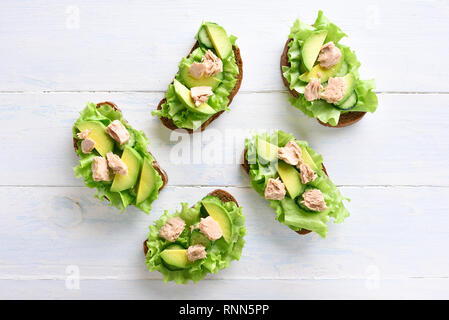 Thunfisch Sandwiches mit Avocado und Salatblätter über hellen Hintergrund. Lecker Thunfisch Brötchen zum Frühstück. Gesunden Snack. Ansicht von oben, flach Stockfoto