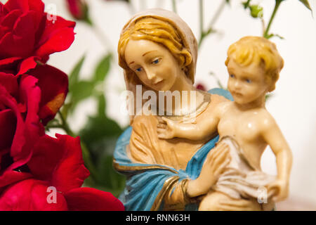 Eine Statue der Jungfrau Maria mit dem Jesuskind in ihren Armen neben einem Blumenstrauß aus Rosen in einer Kapelle. Stockfoto