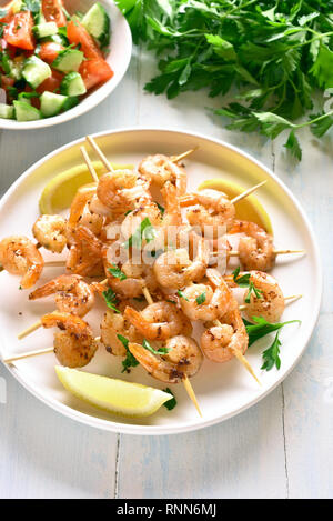 Garnelen Spieße. Gegrillte Garnelen Spieße mit grünen, Gewürzen und Zitrone auf weiße Platte über Holz- Tabelle. Köstliche Meeresfrüchte. Gesunden Snack. Stockfoto