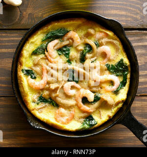 In der Nähe von Pilzen und Spinat frittata mit Garnelen in einer Pfanne auf Holz- Hintergrund. Ansicht von oben, flach Stockfoto