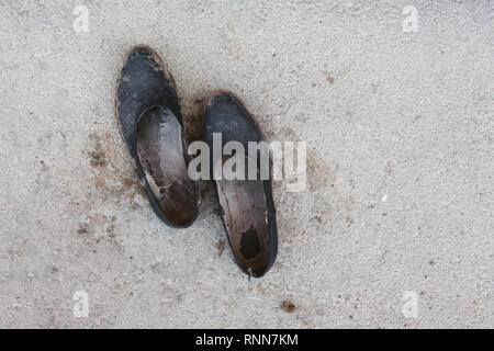 Detailansicht eines alten und schmutzigen Schuhe aus Gummi auf dem Asphalt, abstrakte Komposition. Stockfoto