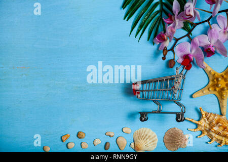 Planen Sie einen Urlaub am Meer. Warenkorb, Muscheln, Seesterne und Blatt der Palme auf einem blauen Hintergrund aus Holz. Stockfoto