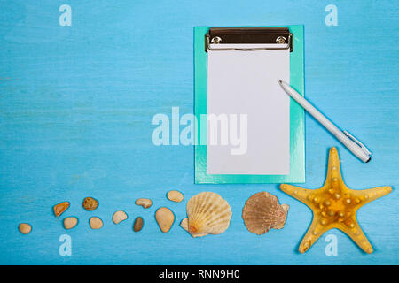 Planen Sie eine Reise zum Meer. Papier, Muscheln und Seesterne auf einem blauen Hintergrund aus Holz. Stockfoto