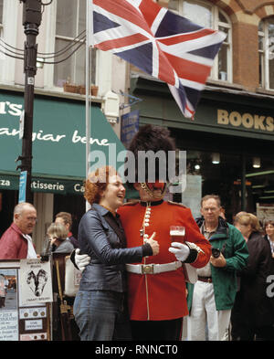 UK. England. Mann verkleidet als Coldstream Guard holding Pint Bier und das Tragen der roten Nase, mit touristischen für Foto zugunsten von Comic Relief posieren. Stockfoto
