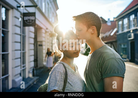 Lächelnde junge Frau geküsst auf der Stirn von ihrem Freund, während sie zusammen auf einer Straße der Stadt am Nachmittag Stockfoto