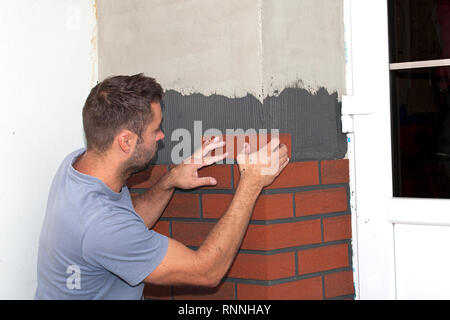 Umbau des Hauses. Arbeiter Ziegel Verkleidung (Nachahmung Ziegel) auf die Außenfassade stecken. Beendigung der Arbeit an der neuen Fassade. Stockfoto