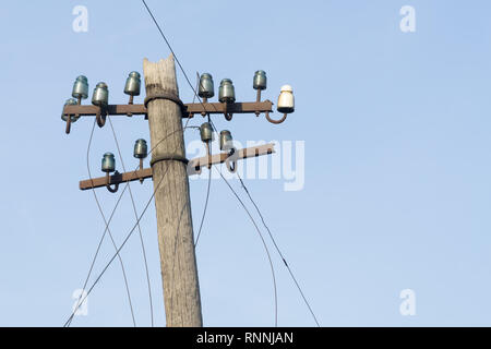 Alte elektrische hölzerne Stange mit Glas und Keramische Isolatoren und Kabel gegen den blauen Himmel. Kopieren Sie Platz. Stockfoto