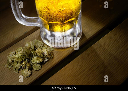 Blick von oben auf eine isolierte gefrorenen Bierkrug auf Holz Tisch, getrocknete Hopfen Blätter Stockfoto