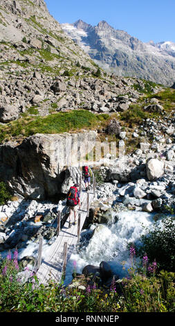 Zwei Wanderer und Bergsteiger Kreuz ein kleiner Bach über eine alte Holzbrücke auf dem Weg zum Base Camp in den Französischen Alpen Stockfoto