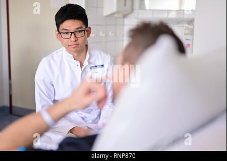 20. Februar 2019, Baden-Wuerttemberg, Heidelberg: biyan Nathanael Harapan, ein praktisches Jahr am Universitätsklinikum Heidelberg, spricht mit einem Patienten in der Chirurgie. Mit dem Masterplan medizinische Studien 2020, die Hochschulen sind neue Wege. Die neu gestaltete ärztliche Untersuchung ist zum ersten Mal der Öffentlichkeit am Universitätsklinikum Heidelberg vorgestellt. Foto: Uwe Anspach/dpa Stockfoto