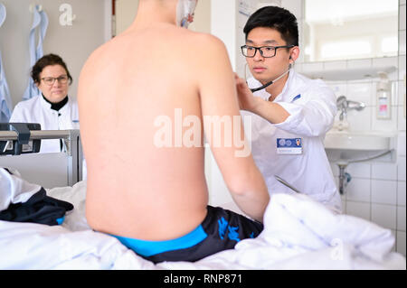 20. Februar 2019, Baden-Wuerttemberg, Heidelberg: biyan Nathanael Harapan (r), ein Student in sein praktisches Jahr am Universitätsklinikum Heidelberg, untersucht einen Patienten in der Chirurgie. Mit dem Masterplan medizinische Studien 2020, die Hochschulen sind neue Wege. Die neu gestaltete ärztliche Untersuchung ist zum ersten Mal der Öffentlichkeit am Universitätsklinikum Heidelberg vorgestellt. Foto: Uwe Anspach/dpa Stockfoto