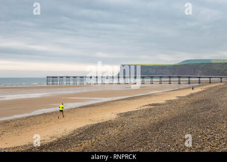 Läufer und Walker Hund am Strand von Saltburn-by-the-Sea, North Yorkshire, England Stockfoto