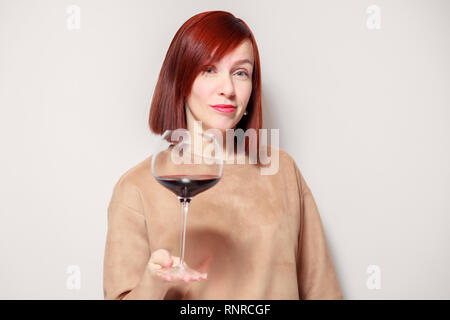 Junge schöne rothaarige Mädchen Sommelier mit Hellen Lippenstift auf weißen Hintergrund ist und lächelnd Glas Rotwein an professionelle blinde Tasten Stockfoto