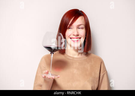 Junge schöne rothaarige Mädchen Sommelier mit Hellen Lippenstift auf weißen Hintergrund ist und lächelnd Glas Rotwein an professionelle blinde Tasten Stockfoto