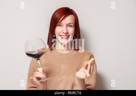 Junge schöne rothaarige Mädchen Sommelier mit Hellen Lippenstift auf weißen Hintergrund ist und lächelnd Glas Rotwein an professionelle blinde Tasten Stockfoto