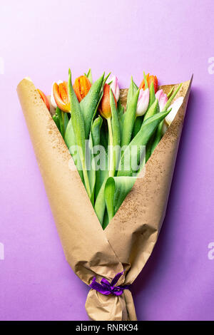 Blumenstrauß aus Tulpen in braunem Papier über rosa Hintergrund gewickelt Stockfoto