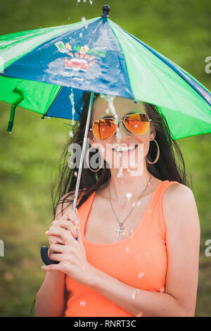 Frau in orange T-Shirt mit Kid Regenschirm unter Regen Stockfoto