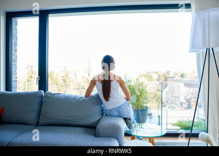 Ansicht von hinten erschossen Der junge Frau Schlafanzüge tragen beim Sitzen auf dem Sofa und schauen aus dem Fenster. Stockfoto