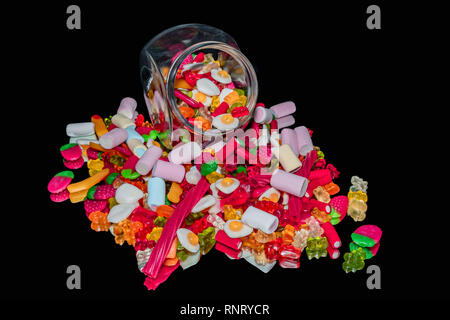 Bunte Bonbons in einem Glas auf einen Spiegel mit einem schwarzen Hintergrund Stockfoto
