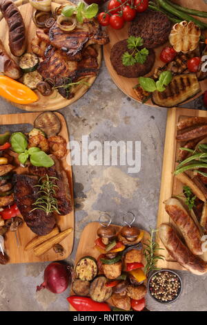 Lecker gegrilltes Fleisch mit Gemüse und Kräutern auf rustikalen Tisch sortiert Stockfoto