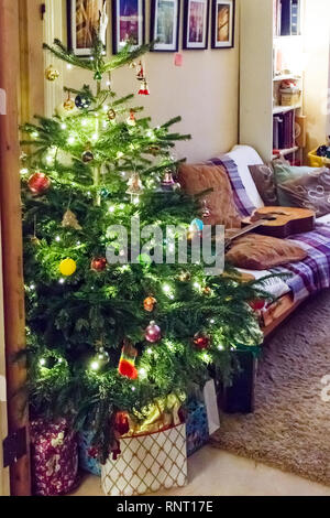 Aufgewickelte Weihnachtsgeschenke durch eine traditionelle Baum mit Lichtern und Kugeln in eine Familie zu Hause, London, UK Stockfoto