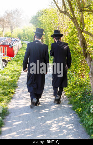 Zwei orthodoxe jüdische Männer, die an einem sonnigen Frühlingsnachmittag in der Nähe von Stamford Hill, London, Großbritannien, den Treidelpfad des Flusses Lea entlang wandern Stockfoto