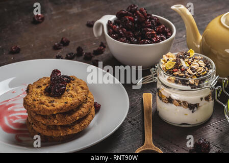 Horizontale Foto mit mehreren Müsli Kekse auf weiße Platte gelegt. Rote Jam ist auf der Platte verschüttet. Trockene rote Cranberries sind in weißen Schale und verschüttete Aro Stockfoto