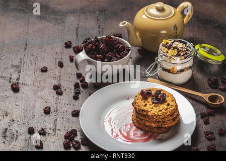 Horizontale Foto mit mehreren Müsli Kekse auf weiße Platte gelegt. Rote Jam ist auf der Platte verschüttet. Trockene rote Cranberries sind in weißen Schale und verschüttete Aro Stockfoto