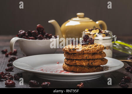 Horizontale Foto mit mehreren Müsli Kekse auf weiße Platte gelegt. Rote Jam ist auf der Platte verschüttet. Trockene rote Cranberries sind in weißen Schale und verschüttete Aro Stockfoto