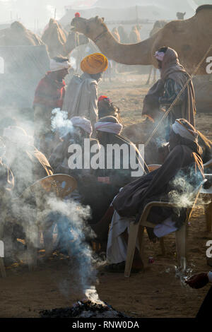 Raika Kamelhirten sitzen Rauchen um ein rauchiges Feuer, während ein kalter Wintermorgen am Pushkar Camel Fair in Rajasthan, Indien Stockfoto