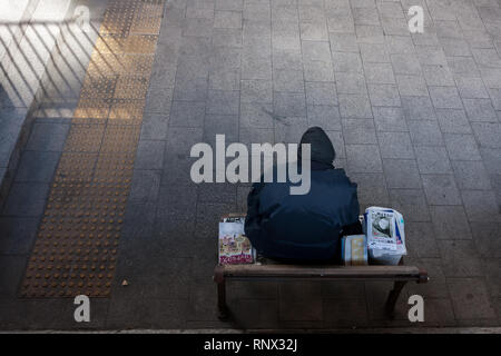 Ein Obdachloser, der liest, während er auf einer Bank in einem kleinen Park in Tokio, Japan, ruht. Stockfoto