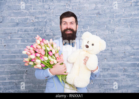 Romantischen Mann. Macho fertig, romantisches Date. Warten auf Darling. Mann gut gepflegt Verschleiß tuxedo Bow Tie halten Blumen Tulpen Bouquet und großen Teddybären Spielzeug. Laden Sie dating. Romantisches Geschenk. Stockfoto