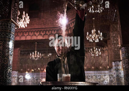 Ein Kellner gießt dampfend heißen süßen Pfefferminztee aus großer Höhe in einem beliebten Restaurant in Marrakesch, Marokko sporting mosaic Säulen und Kronleuchtern. Stockfoto